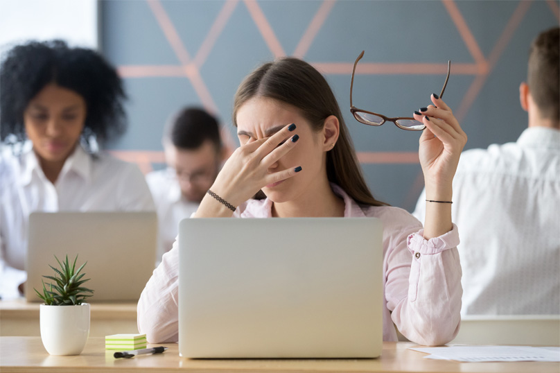 A stressed young woman massaging her eyes while holding her eyeglasses