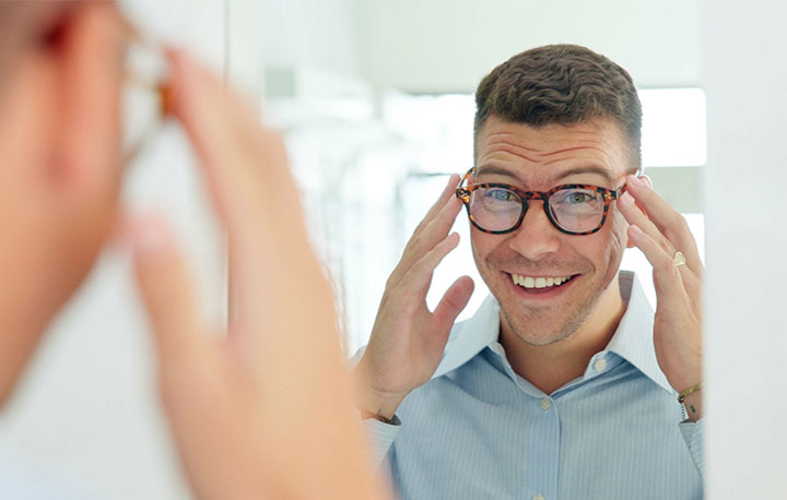 Smiling man trying on eyeglasses while looking in a mirror at an eyewear store
